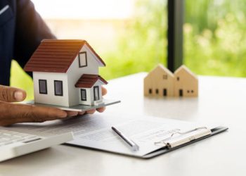 A real estate agent offers a sample home insurance home to sign the agreement. with documents of the contract of sale or lease
