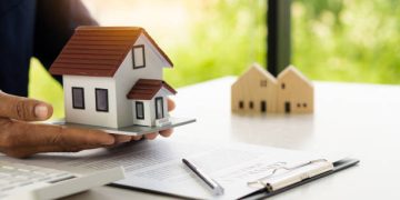 A real estate agent offers a sample home insurance home to sign the agreement. with documents of the contract of sale or lease